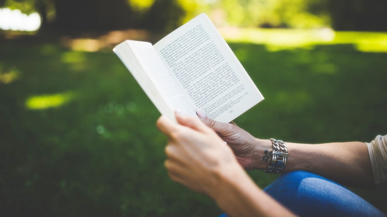 Imagem mostra as mãos de uma mulher segurando um livro aberto.